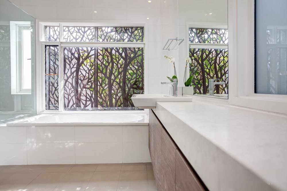 Modern bathroom interior featuring a bathtup, large mirror, and a window with decorative tree-patterned glass.