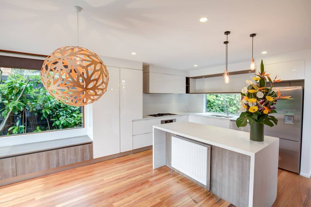 Modern kitchen with a stylish pendant light, an island countertop, and large windows showcasing greenery outside.