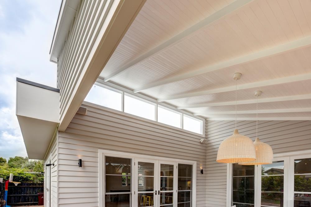 Interior view of a modern home showcasing a high ceiling with white beams, large windows, and two hanging woven pendant lights.