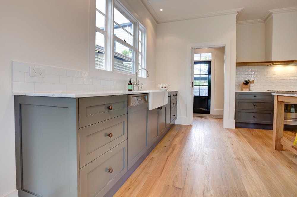 Modern kitchen interior featuring gray cabinets, a white countertop, and wooden floors with natural lighting from windows.