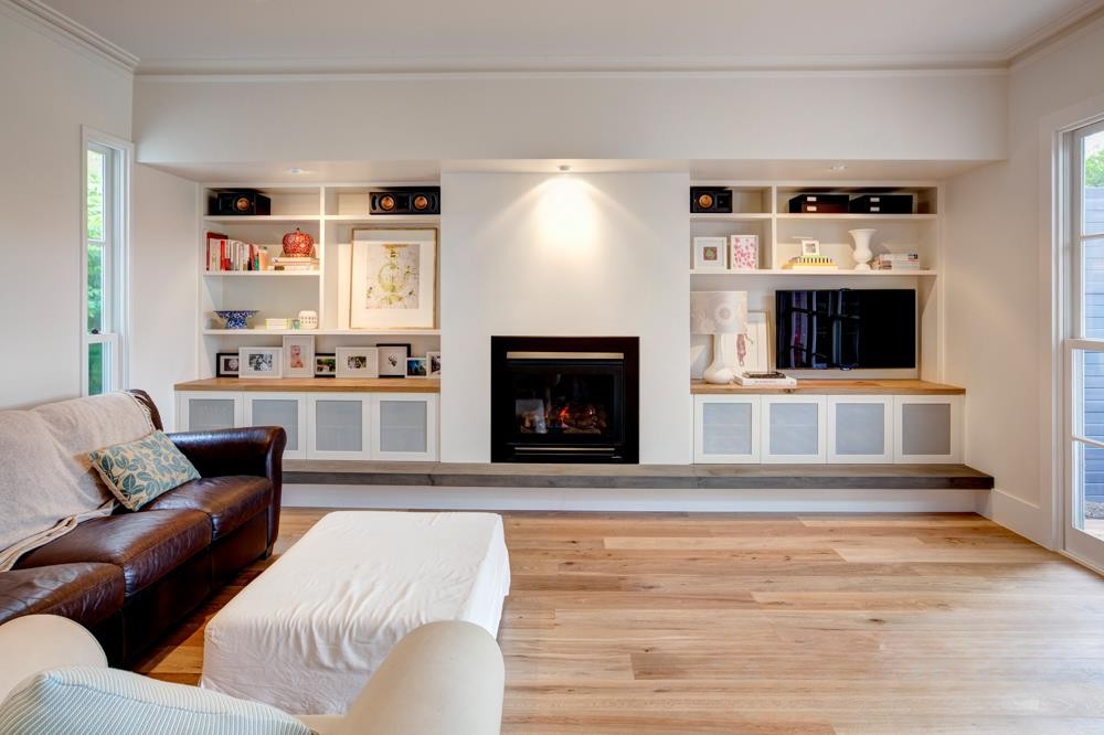 Modern living room with a brown leather sofa, light-colored walls, a fireplace, and built-in shelves displaying books and decorative items.
