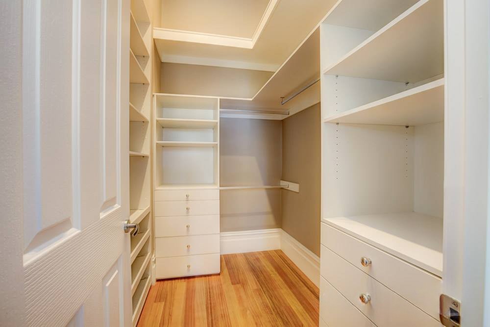 Interior view of a spacious walk-in closet featuring built-in shelves and drawers, with wooden flooring and white walls.
